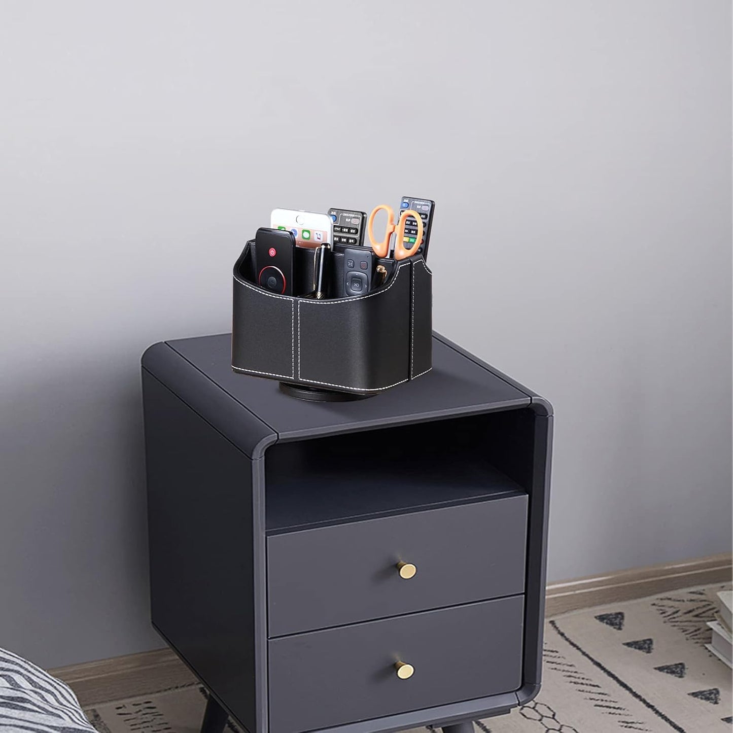 Leather remote control holder with 360° spinning design, for TV remotes, pens, phones, and media accessories on a bedside table.