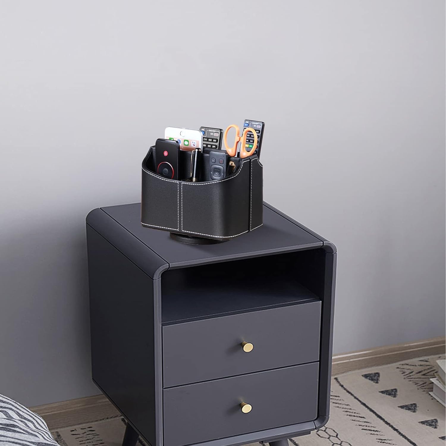 Leather remote control holder with 360° spinning design, for TV remotes, pens, phones, and media accessories on a bedside table.